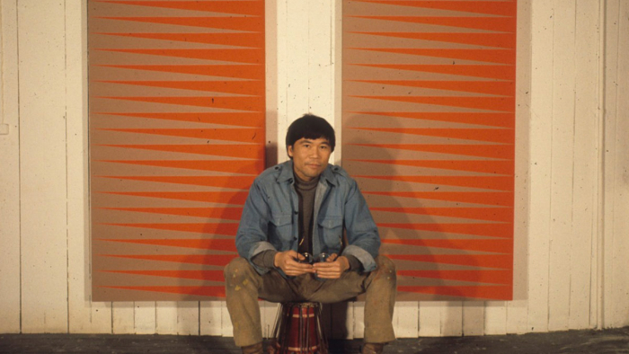 Man with Asian features sits in front of windows.